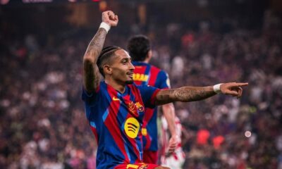 Jogador Raphinha, do Barcelona, celebra no campo com os braços levantados em um estádio