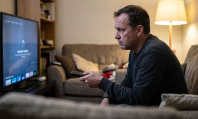 Homem de meia-idade no sofá segurando controle, olhando TV com tela de carregamento