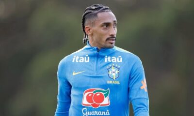 Raphinha, com tranças e bigode, em camisa de treino azul da Seleção Brasileira com logos Itaú e Guaraná