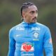 Raphinha, com tranças e bigode, em camisa de treino azul da Seleção Brasileira com logos Itaú e Guaraná