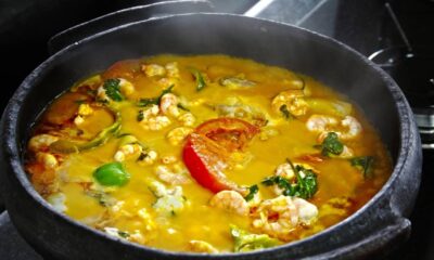 Moqueca de camarão com pimentões coloridos e coentro em panela de barro, com vapor visível