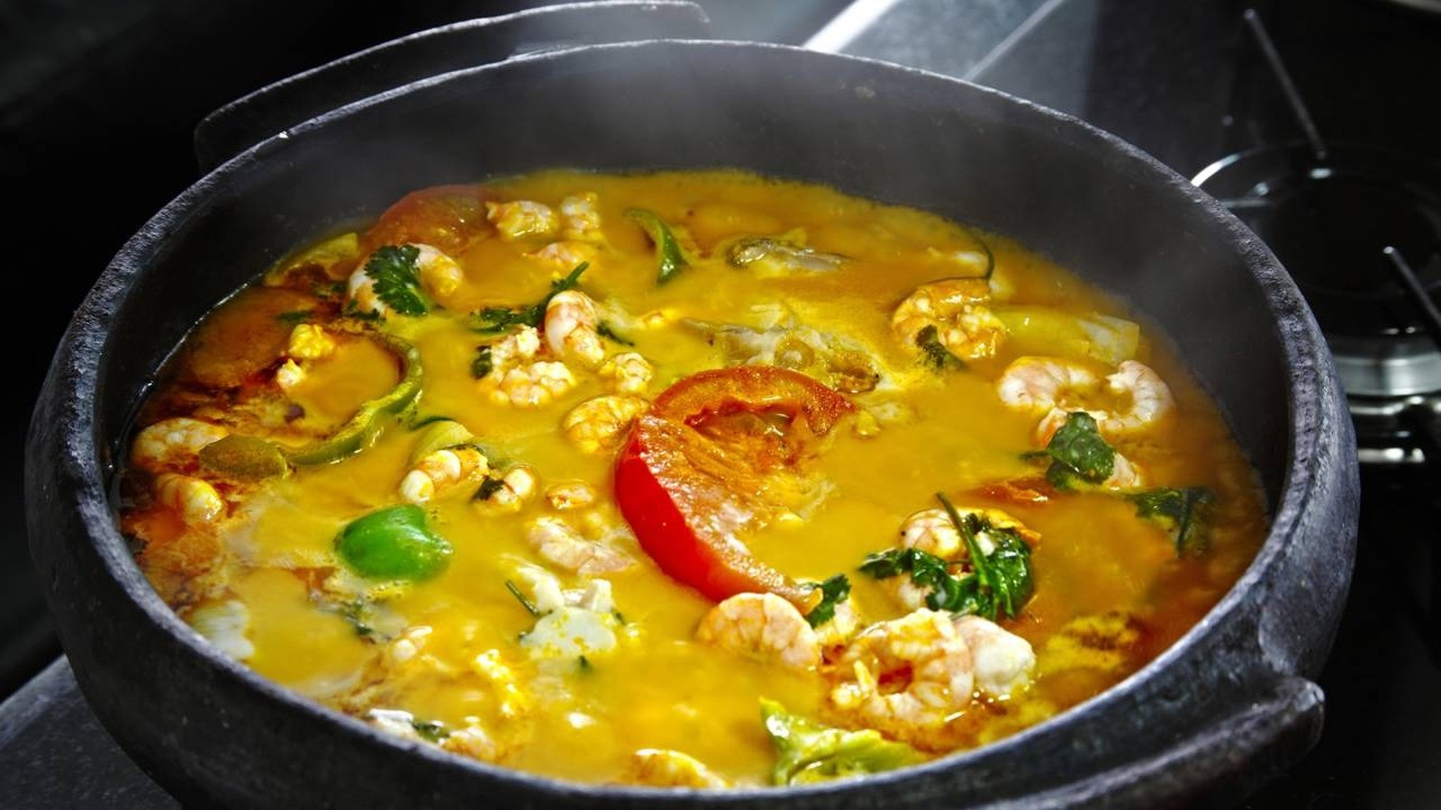 Moqueca de camarão com pimentões coloridos e coentro em panela de barro, com vapor visível