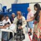 Idosa sorridente em vestido floral com polegar para cima em seção eleitoral com pessoas