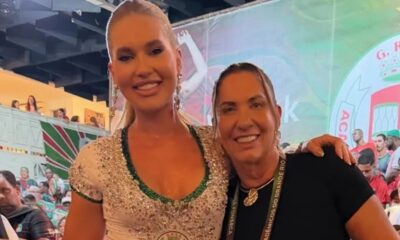 Duas mulheres sorridentes, uma loira em vestido brilhante e outra com crachá Grande Rio