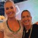 Duas mulheres sorridentes, uma loira em vestido brilhante e outra com crachá Grande Rio