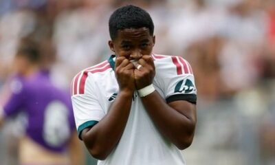 Jovem jogador de futebol, Endrick, com as mãos na boca, em campo com camisa branca