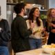 Mulher com xícara observa grupo de quatro pessoas conversando animadamente em ambiente social
