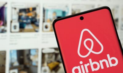 Smartphone exibe o logotipo e o nome 'airbnb' em branco sobre um fundo vermelho vibrante na tela