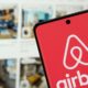 Smartphone exibe o logotipo e o nome 'airbnb' em branco sobre um fundo vermelho vibrante na tela