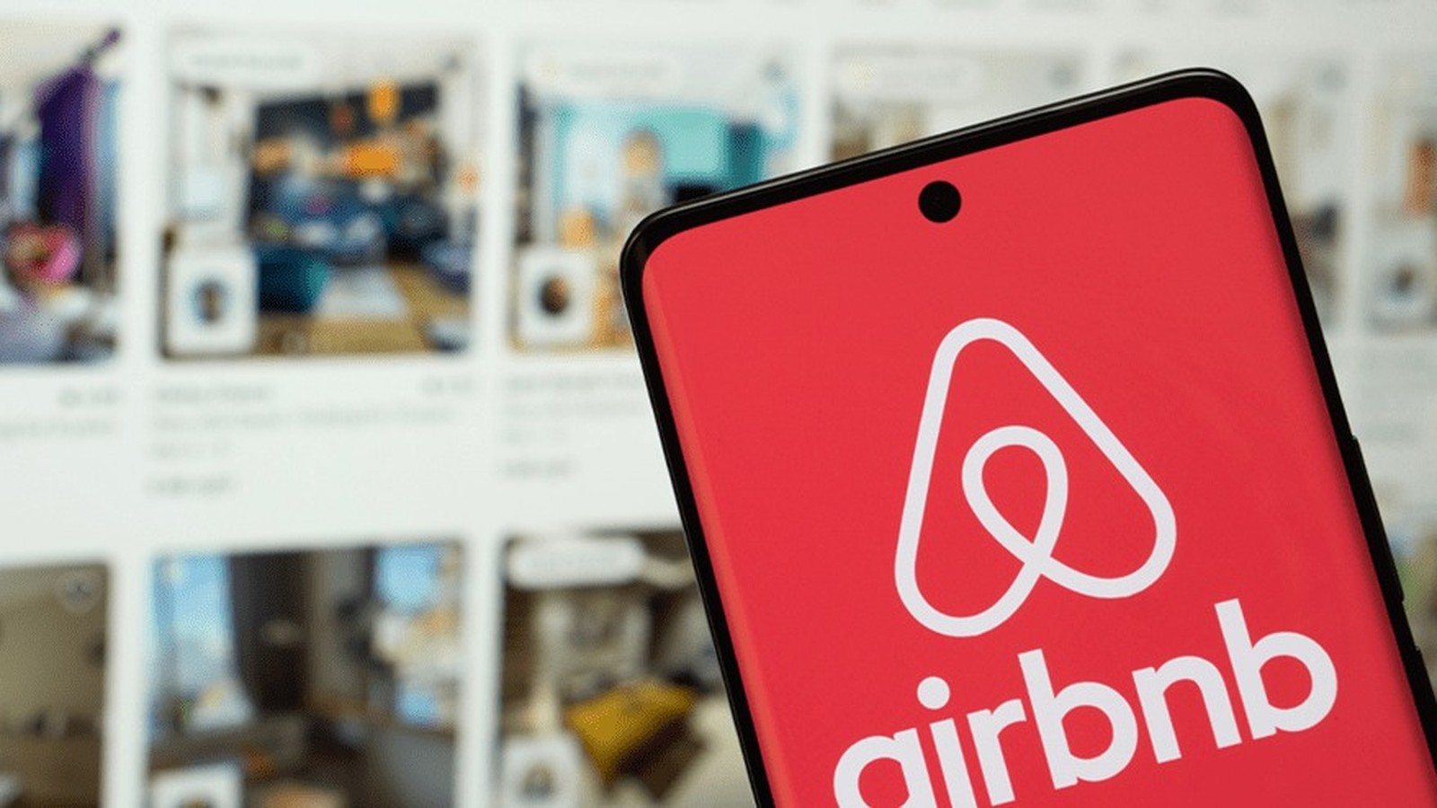 Smartphone exibe o logotipo e o nome 'airbnb' em branco sobre um fundo vermelho vibrante na tela