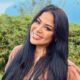 Gisele Nascimento sorri, cabelos escuros, em ambiente externo com folhagem verde