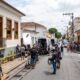 Equipe de filmagem em rua com câmera em trilhos, prédio, vans, pessoas e padaria