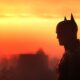 Batman em silhueta, perfil, contra um vibrante céu de pôr do sol laranja e vermelho