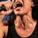 Cantora suada com boca aberta cantando no microfone, músculos do pescoço visíveis
