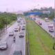 Wet highway traffic: cars, trucks (one 'NUTRYMAX'), motorcycles, and green roadside