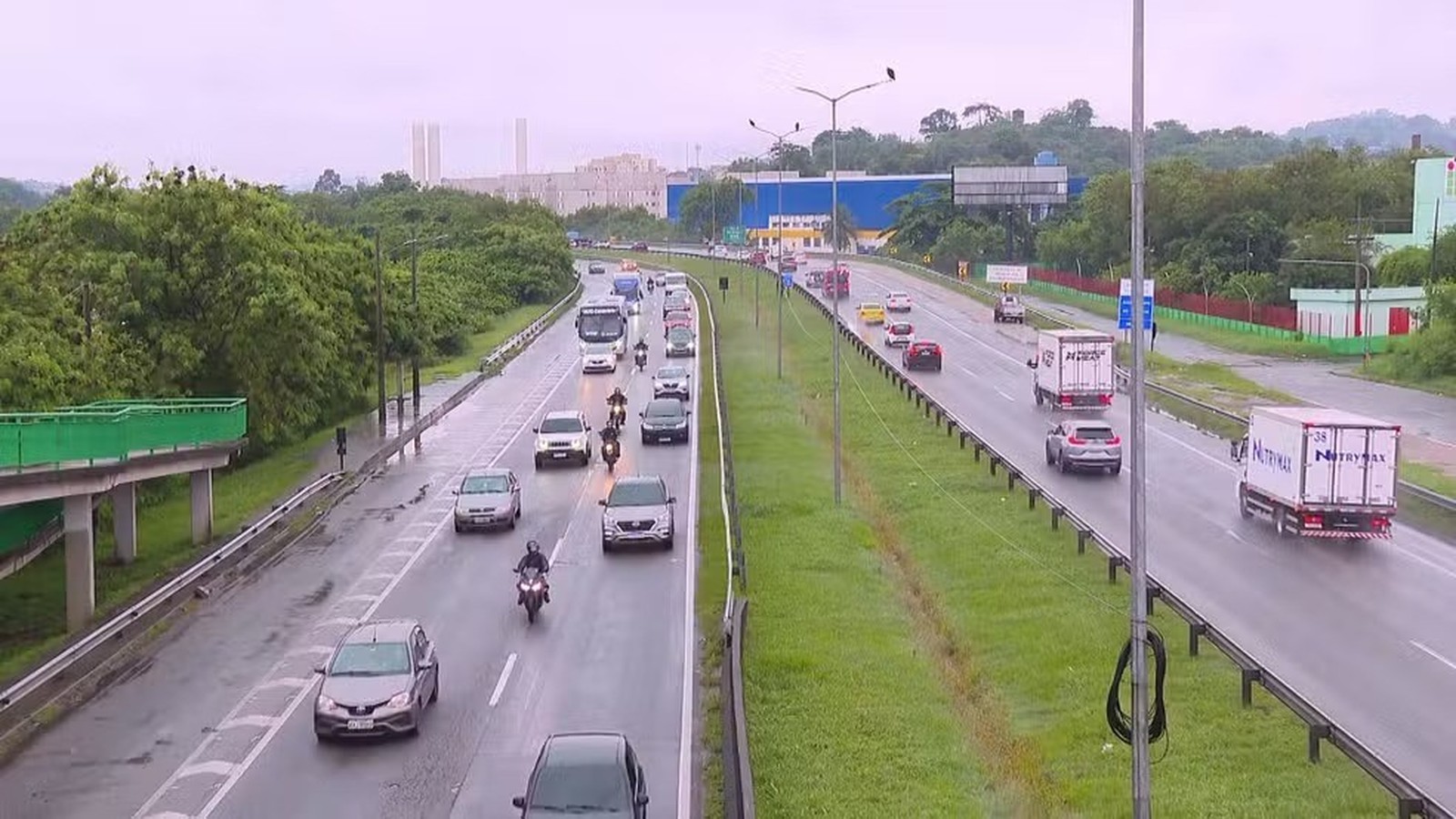 Wet highway traffic: cars, trucks (one 'NUTRYMAX'), motorcycles, and green roadside