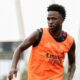 Vini Jr. em campo, usando colete de treino laranja com "Emirates FLY BETTER", olhando para a direita