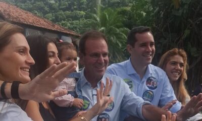 Eduardo Paes e família sorrindo, acenando, com broches de campanha '5' e '555'