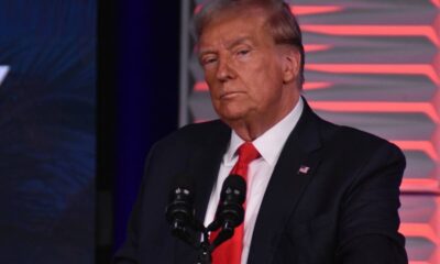 Donald Trump de terno escuro e gravata vermelha em pódio com microfones