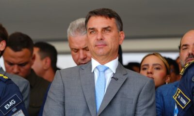Flávio Bolsonaro de terno e gravata azul claro, cercado por outras pessoas em evento