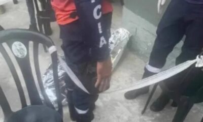 Pessoa uniformizada perto de corpo embrulhado em prata no chão, com fitas e cadeiras