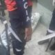 Pessoa uniformizada perto de corpo embrulhado em prata no chão, com fitas e cadeiras