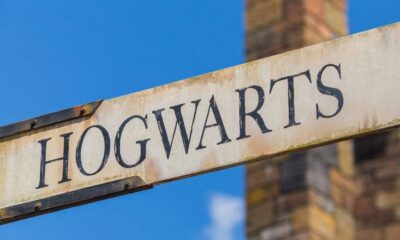 Sinal de madeira antigo com a palavra HOGWARTS em letras escuras, sob céu azul
