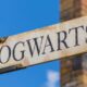 Sinal de madeira antigo com a palavra HOGWARTS em letras escuras, sob céu azul