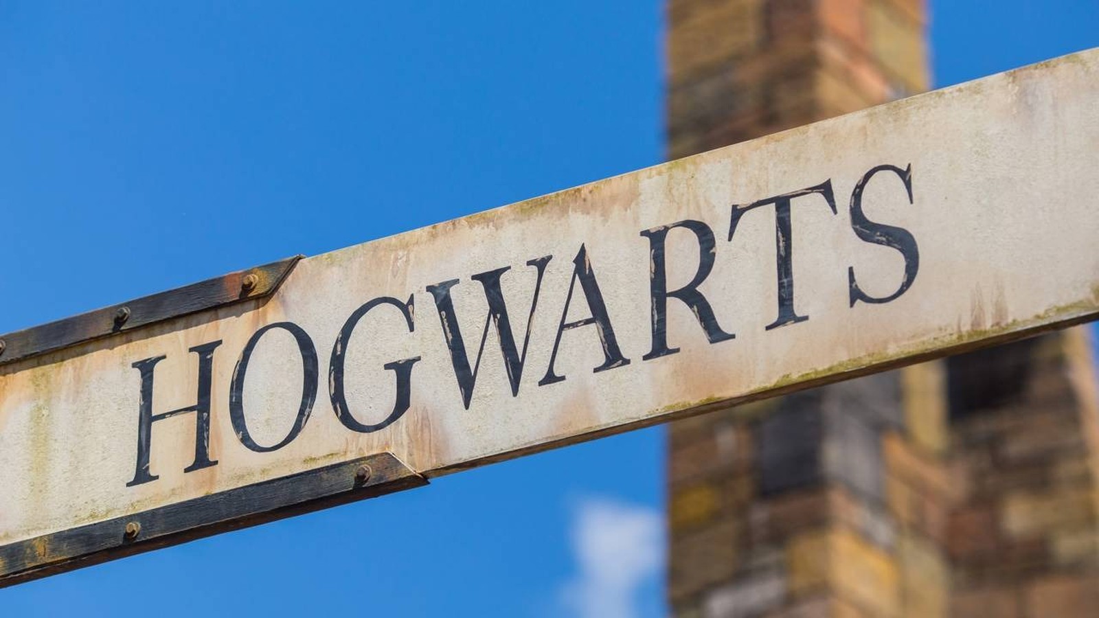 Sinal de madeira antigo com a palavra HOGWARTS em letras escuras, sob céu azul