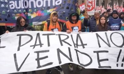Grupo de manifestantes segura banner branco com "LA PATRIA NO SE VENDE!!!" e "autonoma" ao fundo