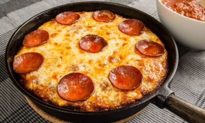 Pizza de pepperoni com queijo derretido em frigideira de ferro fundido, ao lado de molho de tomate