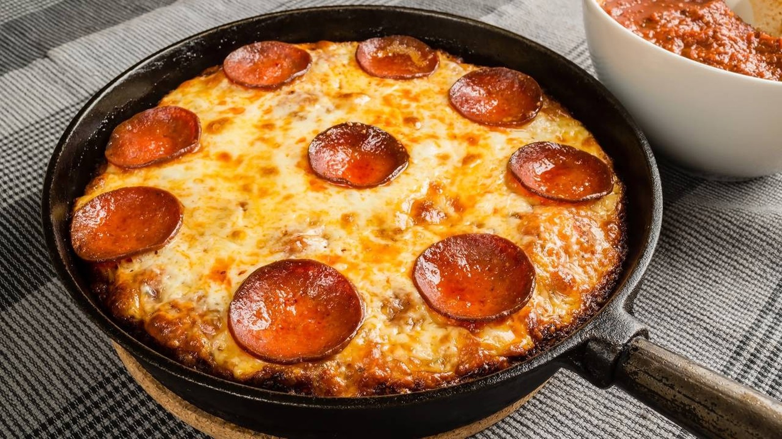 Pizza de pepperoni com queijo derretido em frigideira de ferro fundido, ao lado de molho de tomate