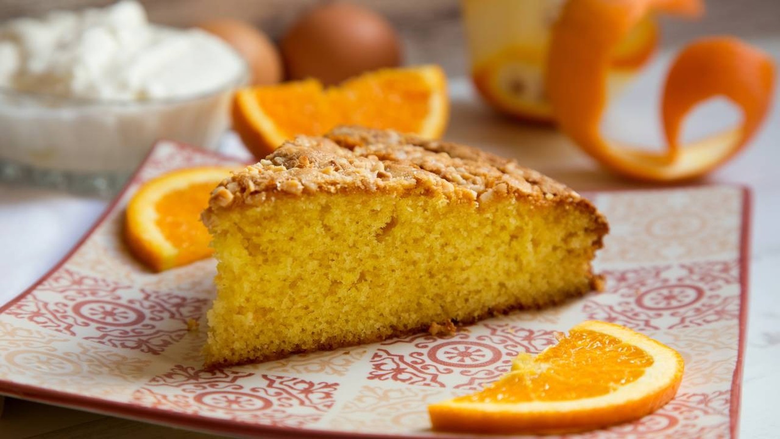 Fatia de bolo de laranja com cobertura crocante, em prato e rodelas de laranja