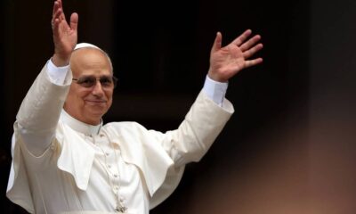 Papa Leão XIV, em vestes brancas, sorri e acena com ambas as mãos