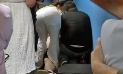 Duas pessoas, uma de calça branca e outra de blusa escura, agachadas prestando socorro