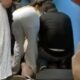 Duas pessoas, uma de calça branca e outra de blusa escura, agachadas prestando socorro