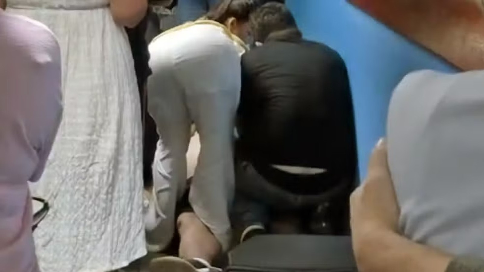 Duas pessoas, uma de calça branca e outra de blusa escura, agachadas prestando socorro