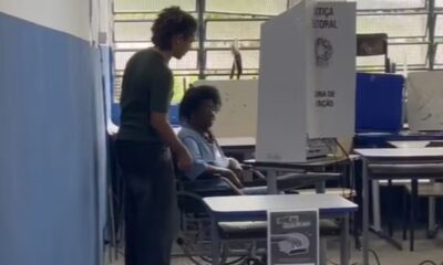 Mulher idosa em cadeira de rodas vota em urna eletrônica, com auxílio