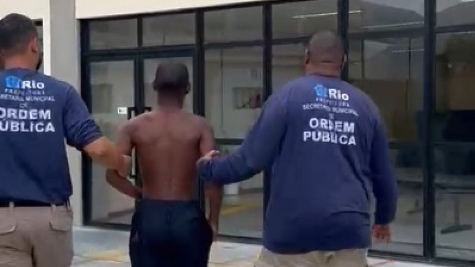 Dois agentes da Ordem Pública escoltam jovem sem camisa. Logos 'Rio Ordem Pública'