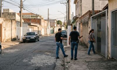 Homens de coletes e mulher em frente a portão de casa em rua