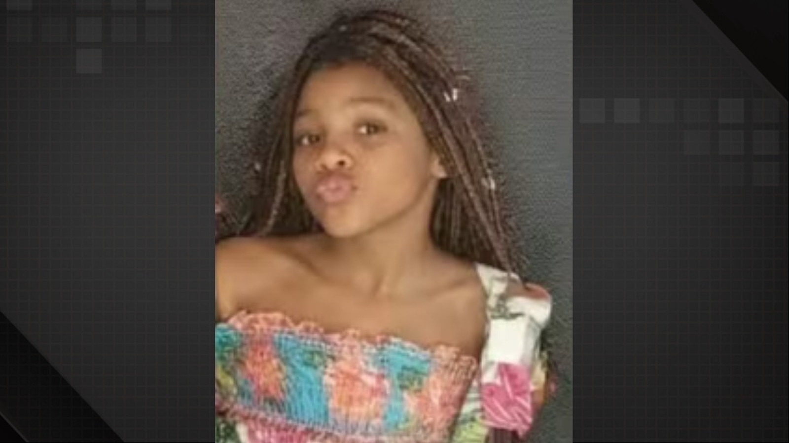 Close-up de uma menina negra com tranças, lábios fazendo bico, vestindo uma blusa colorida