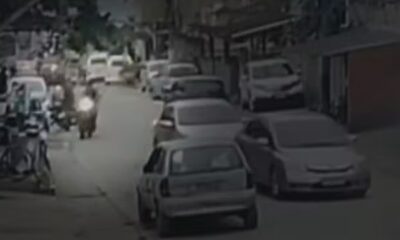 Imagens de segurança de rua com carros estacionados, pedestres e uma motocicleta em movimento