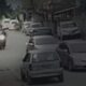 Imagens de segurança de rua com carros estacionados, pedestres e uma motocicleta em movimento