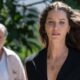Nathalia Dill séria em primeiro plano com colar, homem desfocado atrás em cenário verde