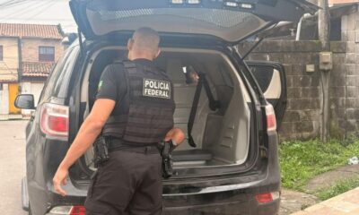 Polícia Federal officer, black uniform, next to open police SUV trunk; person visible inside