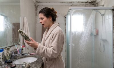 Mulher em roupão chocada segurando frasco mofado em banheiro com mofo nas paredes e teto