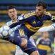 Três jogadores de futebol disputam uma bola em campo, um de uniforme azul e amarelo, dois de listras claras.