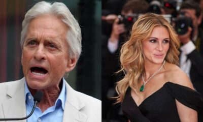 Michael Douglas, cabelos brancos, falando ao microfone e Julia Roberts, cabelo loiro, usando colar de esmeralda