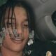 Oruam, homem jovem, dreadlocks com miçangas, sorri levemente dentro de um carro. Usa anéis