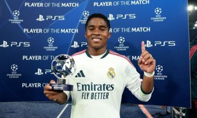 Jogador Endrick sorri segurando troféu de Melhor em Campo da Champions League em fundo azul
